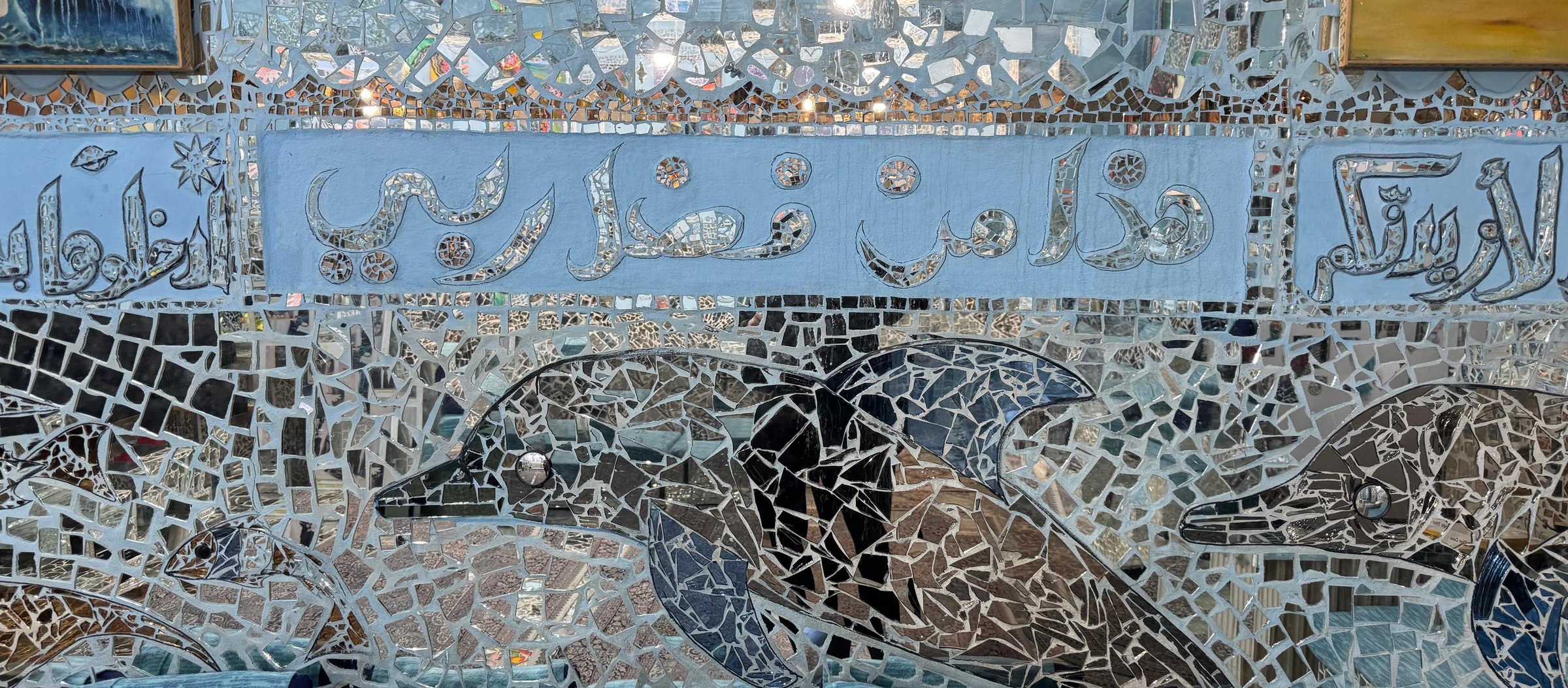 Mirror-mosaic dolphins beneath a band of calligraphy in the Sea World Hall