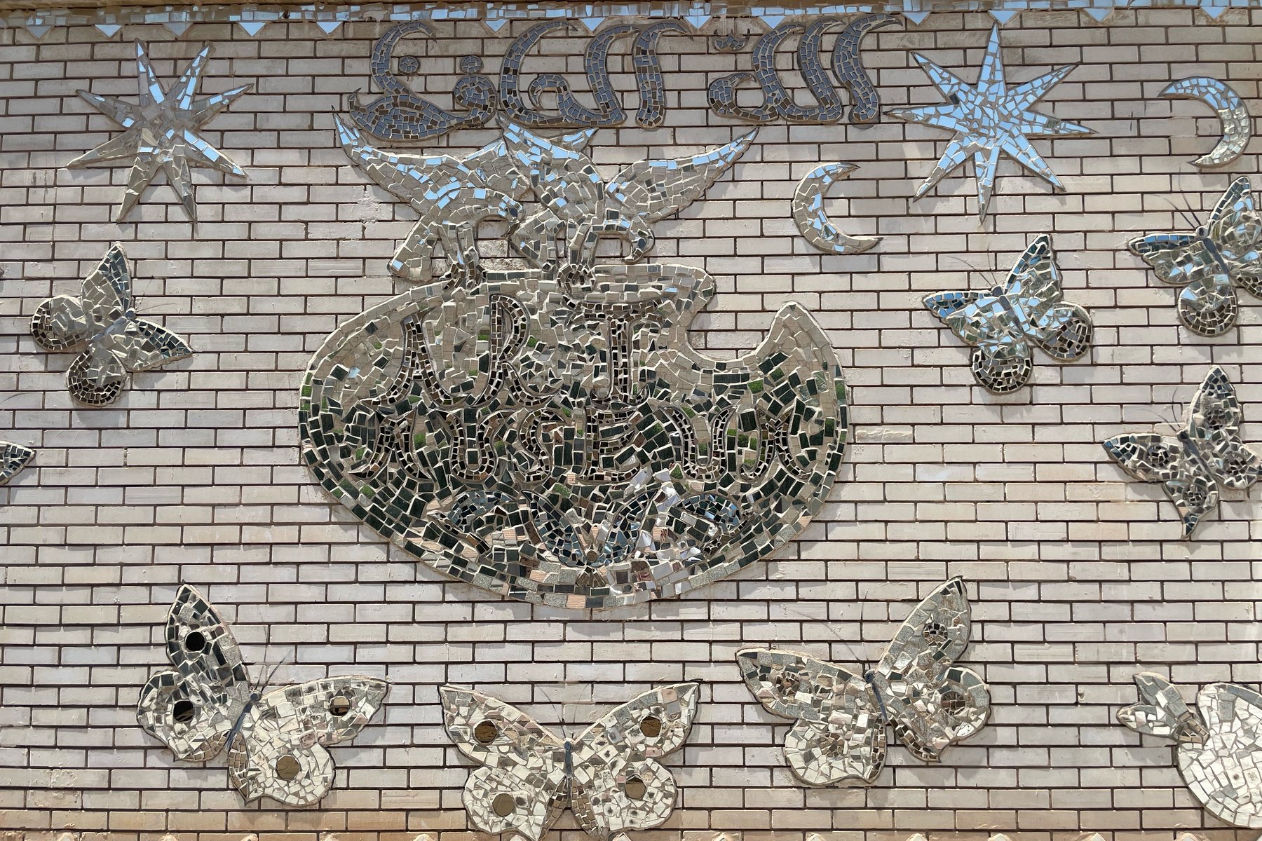 Mirror-mosaic butterflies and stars around a calligraphy medallion on the garden wall
